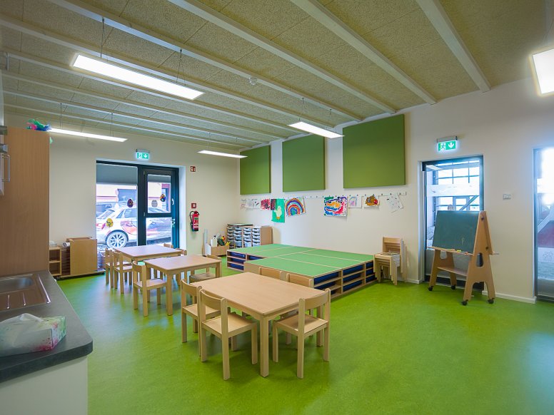 Group room of a day care centre with green floor and wooden tables and chairs